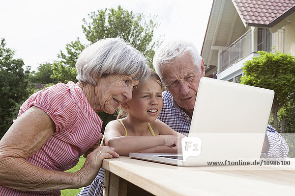 Großeltern und Enkelin mit Laptop im Garten