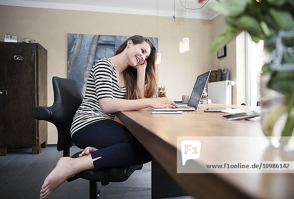 Lächelnde Frau sitzt auf dem Gesundheitssessel am Schreibtisch mit Laptop