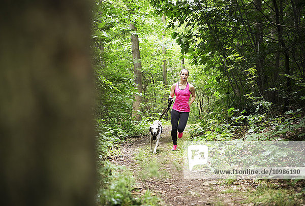 Junge Frau beim Joggen mit Hund im Wald