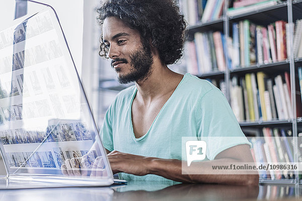 Junger Mann  der in der Bibliothek arbeitet  mit einem futuristischen Computer.