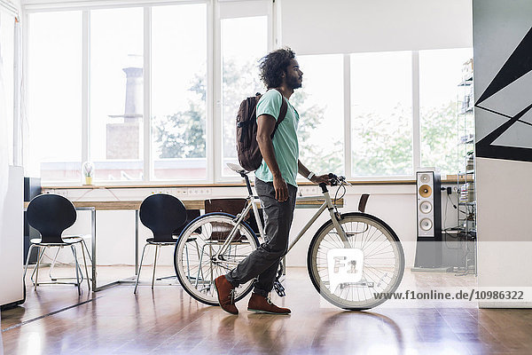 Junger Mann mit Rucksack schiebt Fahrrad im Büro