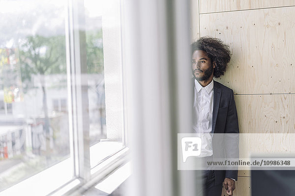 Young businessman standing by window  thinking