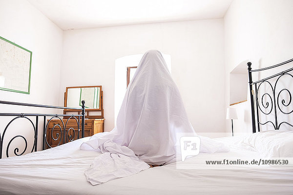 Woman with bed sheet sitting on bed