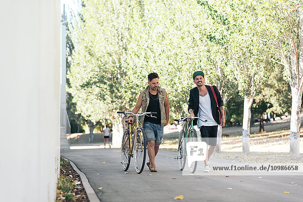 Zwei Männer  die mit Fahrrädern im Park spazieren gehen.