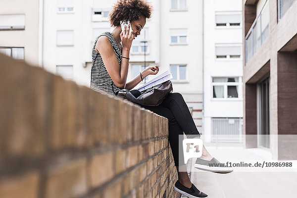 Young woman sitting on wall telephoning with cell phone