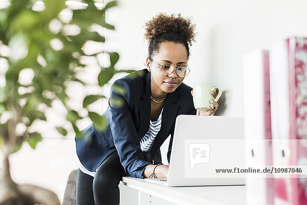 Geschäftsfrau mit Tasse Kaffee beim Blick auf den Laptop