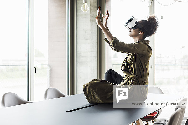 Frau im Büro sitzend auf dem Konferenztisch mit Virtual-Reality-Brille
