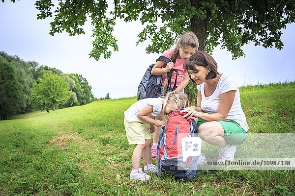 Mutter und Töchter auf der Wiese beim Wandern  Blick in den Rucksack