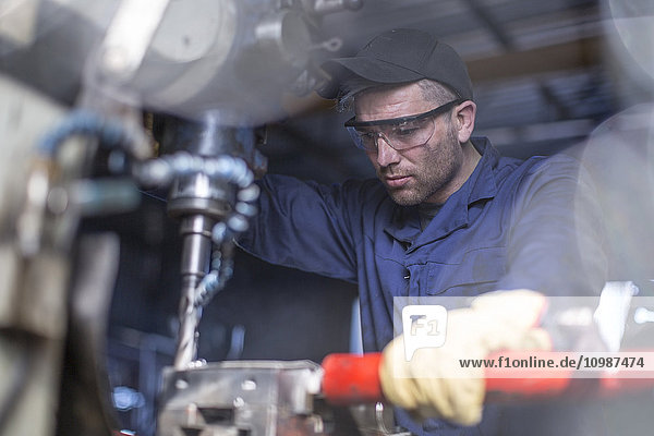 Mechaniker trägt Schutzbrille mit Bohrmaschine in der Werkstatt