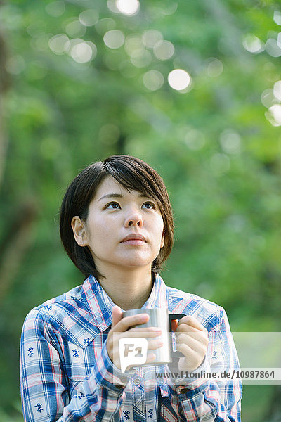 Junge Japanerin beim Kaffeetrinken auf einem Campingplatz