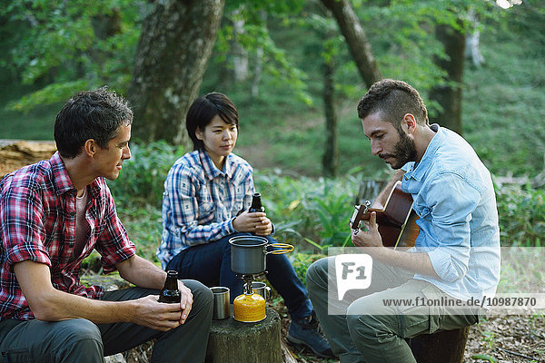 Multi-ethnic group of friends playing guitar at a camp site