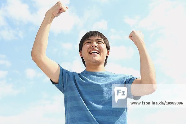 Young Japanese man cheering against blue sky