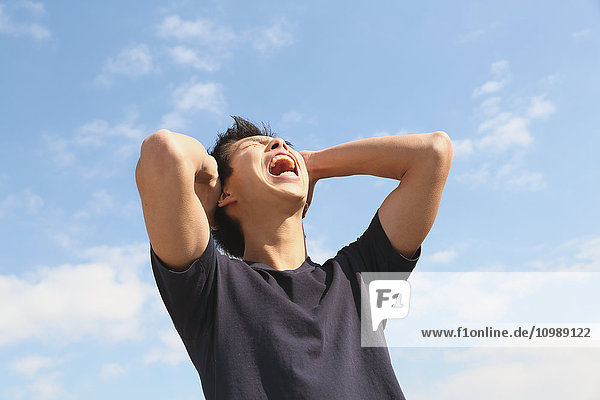 Junger japanischer Mann jubelt vor blauem Himmel