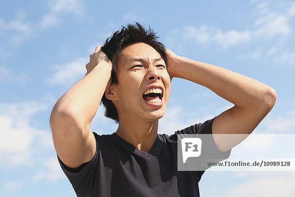 Junger japanischer Mann jubelt vor blauem Himmel