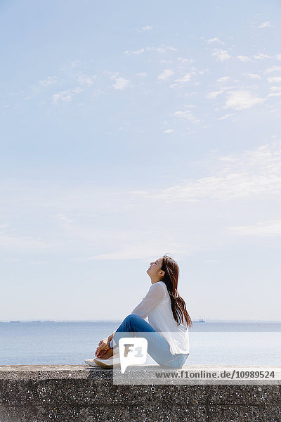 Junge japanische Frau sitzt auf einer Betonmauer am Meer