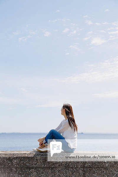 Young Japanese woman sitting on concrete wall by the sea