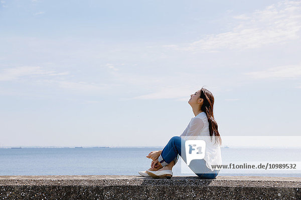 Young Japanese woman sitting on concrete wall by the sea