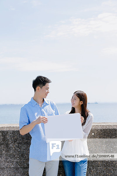 Junges japanisches Paar mit Whiteboard am Meer