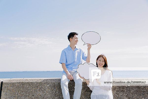 Junges japanisches Paar mit Anzeigetafeln am Meer