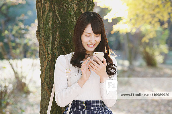 Junge Japanerin mit Smartphone in einem Stadtpark