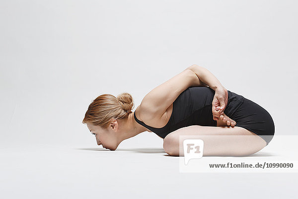 Attractive young Japanese woman wearing black pants and tank top practicing yoga on white background
