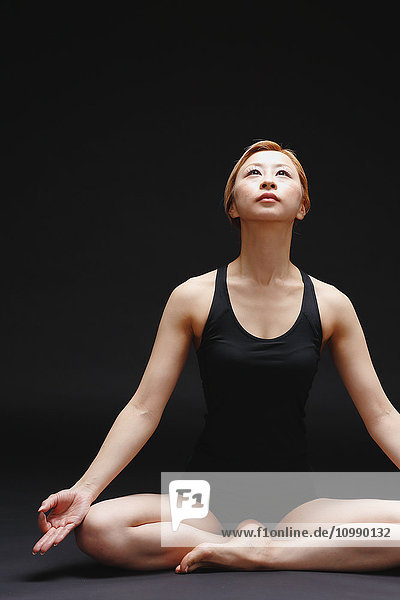 Attractive young Japanese woman wearing black pants and tank top practicing yoga on black background