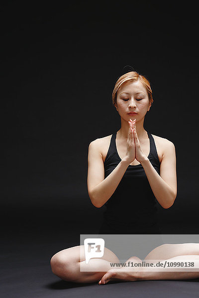 Attraktive junge Japanerin in schwarzer Hose und Tanktop übt Yoga auf schwarzem Hintergrund