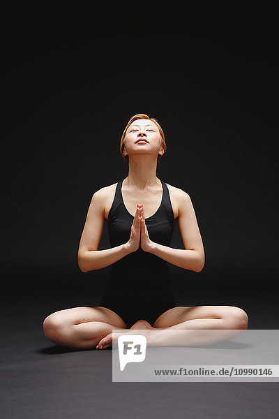 Attractive young Japanese woman wearing black pants and tank top practicing yoga on black background