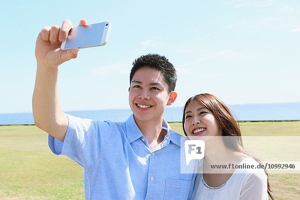 Junges japanisches Paar macht Selfie am Meer