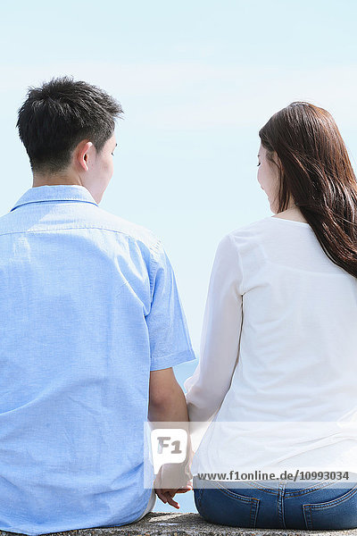 Junges japanisches Paar sitzt auf einer Betonmauer am Meer
