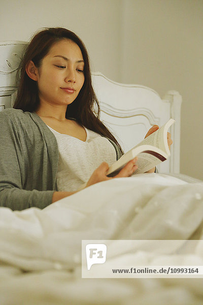 Young attractive Japanese woman reading in bed