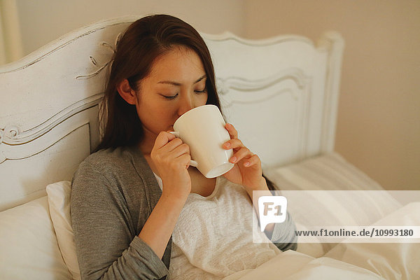 Young attractive Japanese woman drinking coffee in bed