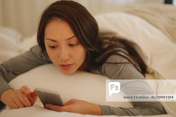 Young attractive Japanese woman with smartphone in bed