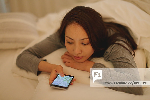 Young attractive Japanese woman with smartphone in bed