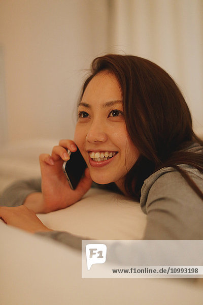 Junge attraktive Japanerin beim Telefonieren im Bett