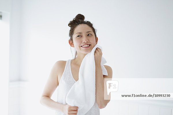 Junge attraktive japanische Frau wischt sich das Gesicht mit einem Handtuch im Badezimmer ab