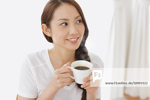 Junge attraktive japanische Frau trinkt Kaffee zu Hause