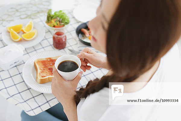 Young attractive Japanese woman having breakfast at home