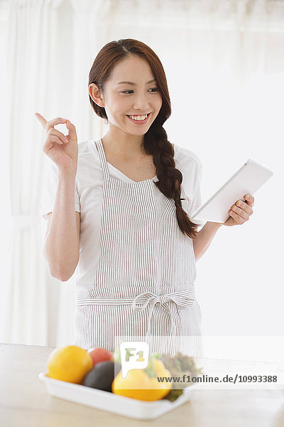 Young attractive Japanese woman cooking at home with tablet