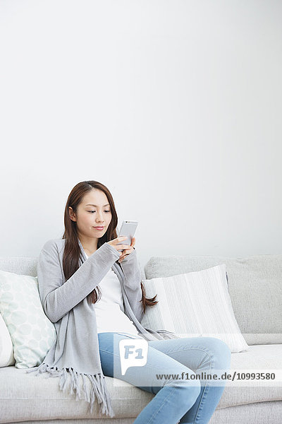 Junge attraktive japanische Frau mit Smartphone auf dem Sofa