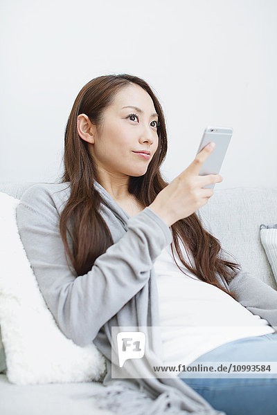 Young attractive Japanese woman with smartphone on the sofa