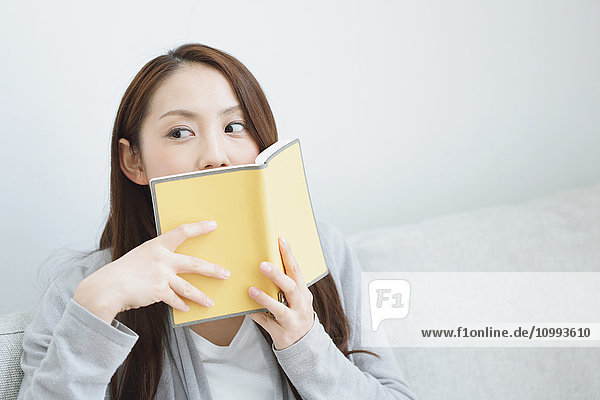 Young attractive Japanese woman with book on the sofa
