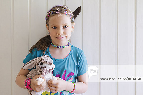 Porträt eines jungen Mädchens  das vor einer Wand steht und seinen Spielzeughasen hält  Schweden