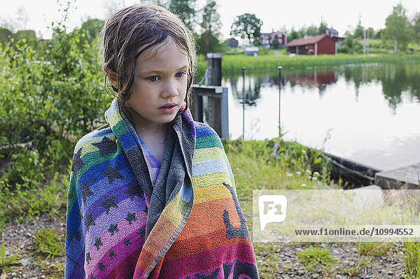 Portrait of girl standing on lakefront daydreaming and wrapped in beach towel  Sweden