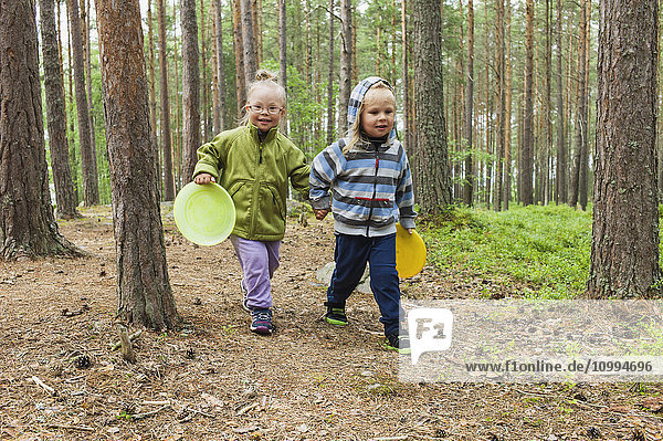 4 Jahre alte Geschwister  die mit ihren Frisbees durch den Wald laufen  Schweden