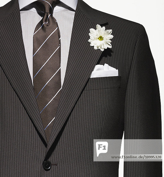 Detail einer braunen Anzugsjacke mit Hemd und Krawatte sowie weißem Einstecktuch und Blume