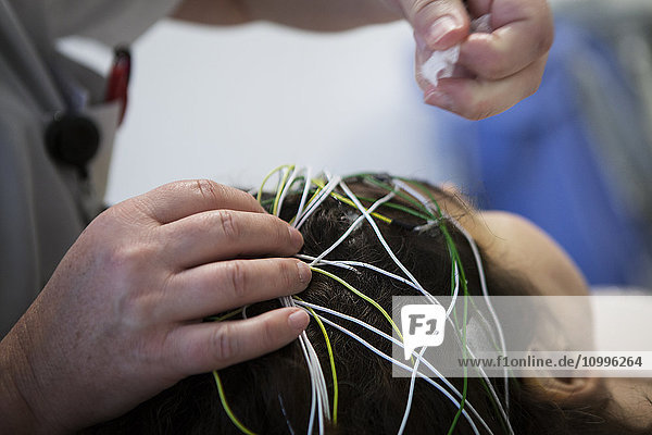 Reportage in einer funktionellen neurologischen Untersuchungseinheit. Epilepsie-Screening und Folgeberatung. Die Patienten machen ein Video-EEG (Elektroenzephalogramm)  bei dem sie verschiedenen akustischen und visuellen Reizen ausgesetzt werden. Die Muster werden anschließend vom Neurologen analysiert. Eine Krankenschwester legt die Elektroden an.