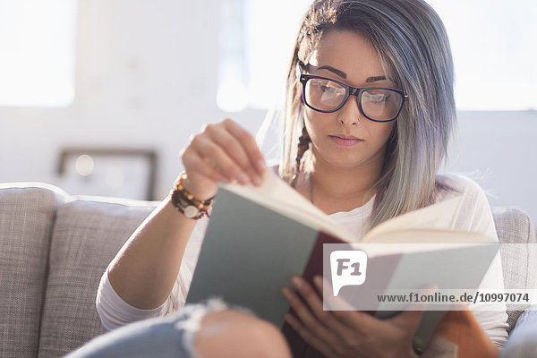 Young woman sitting on sofa and reading book