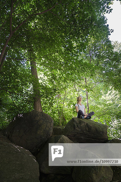Young woman meditating on rocks in woodland