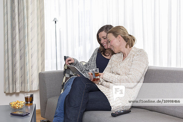 Frauen sitzen lachend auf dem Sofa und schauen auf ein Tablet